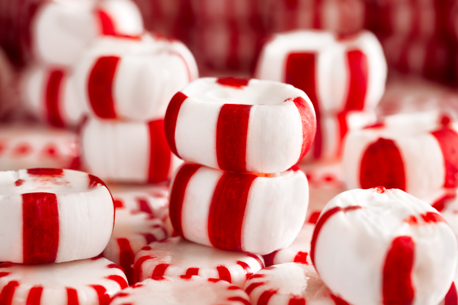 This Brian Charles Steel photograph is composed entirely of red and white peppermints. The ground and background are made of white wheel shaped peppermints each with twelve red stripes. On top of those mints are larger oval shaped red and white mints. In the foreground there is a larger mint in the bottom right corner angled toward the top left corner. Aligned with that angle are three stacks of two larger mints creating a diagonal line all the way to the top left corner. On the bottom left side there is a single large mint with one end of it going out of frame.  